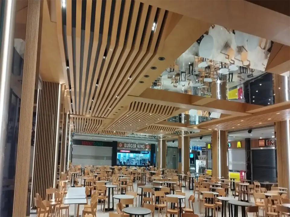 Yemek alanı tavanında birbirine yaklaşan ahşap çıta hatları ve önde beyaz masalar