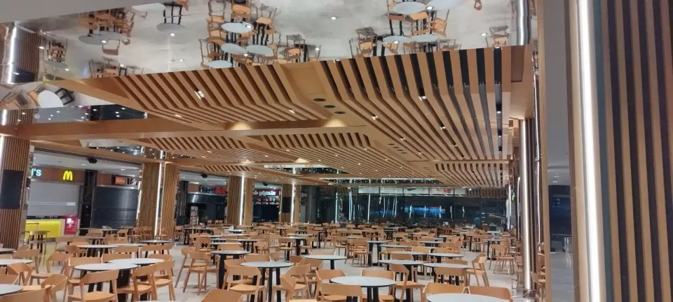 Aynalı tavan yüzeyi ve dalgalı ahşap çıtaların altında sıralanan masa sandalyeler