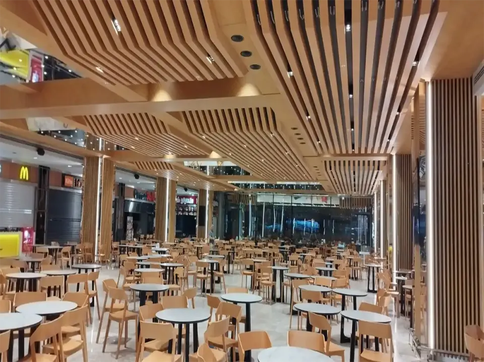 Kavisli ahşap çıtalı tavan altında cam cepheye uzanan beyaz yuvarlak masalı oturma alanı