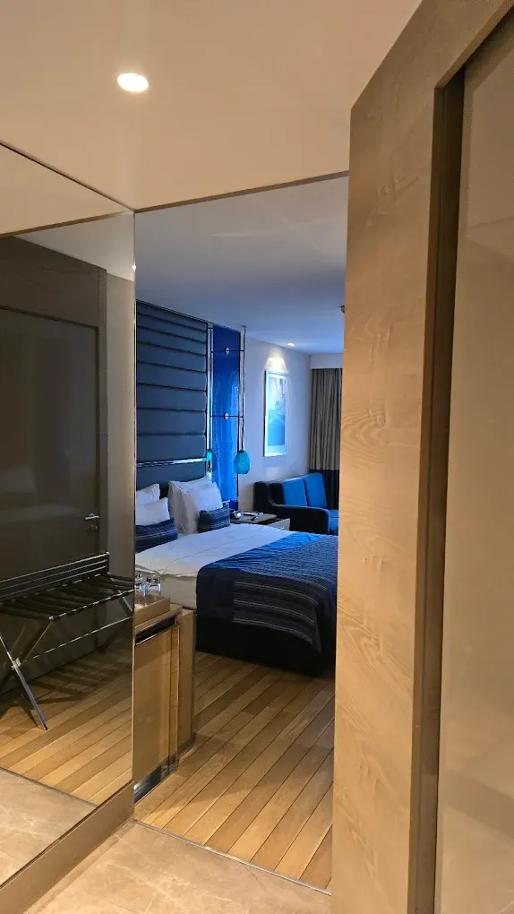 Kayak tesisi otel odası örneğinde ahşap kaplamalı giriş, mavi yatak başlığı ve koltuk